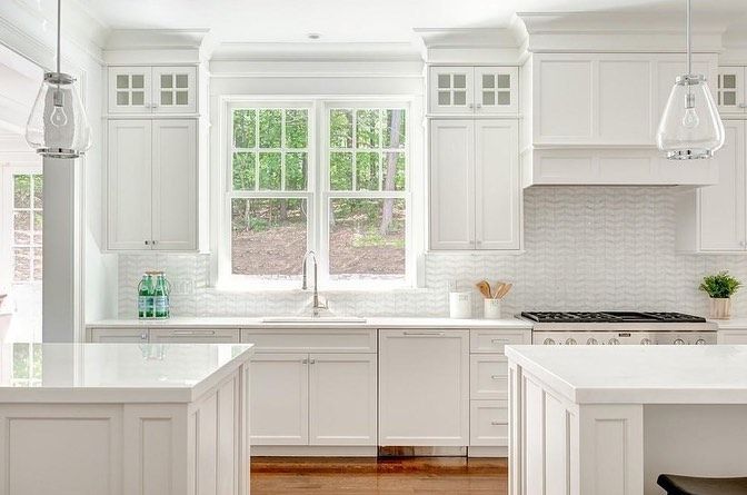 A kitchen with white cabinets , a stove , a sink , and two windows.