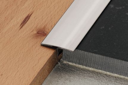 A stainless steel trim is between a wooden floor and a tile floor.