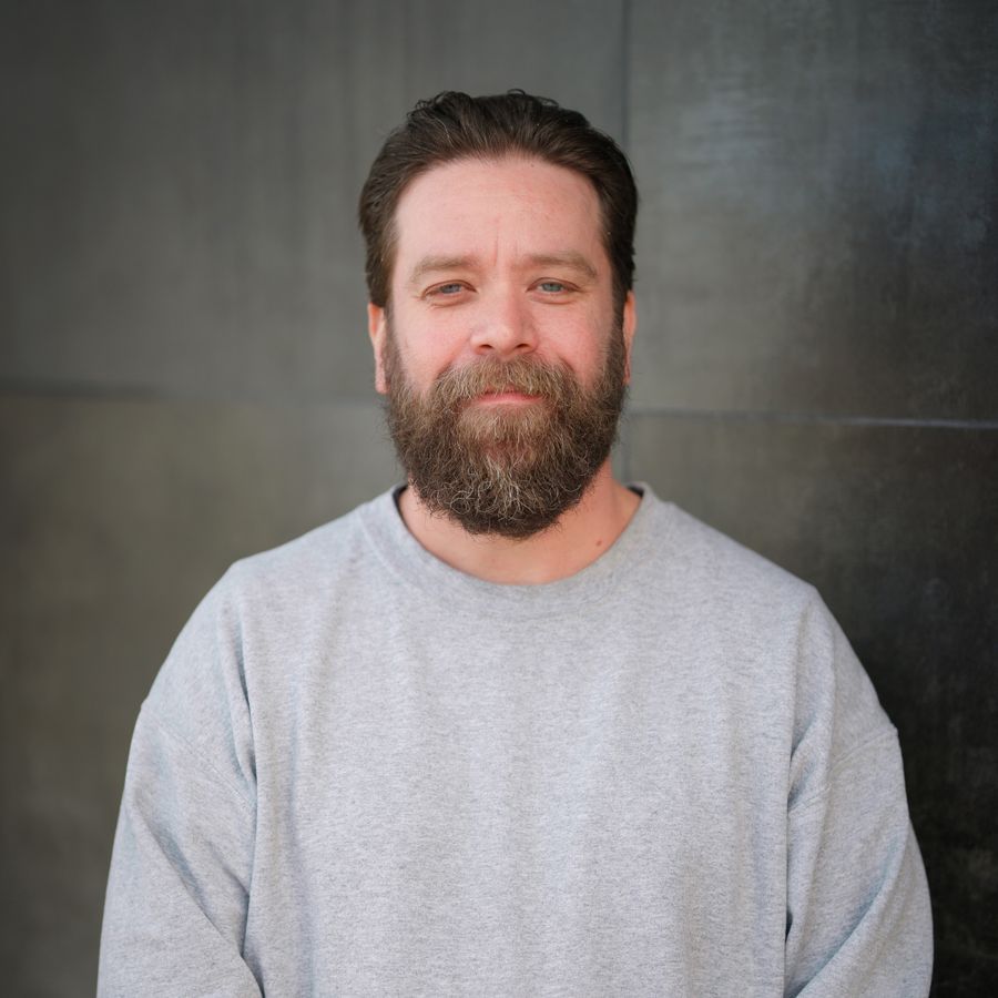 A man with a beard is wearing a grey sweater