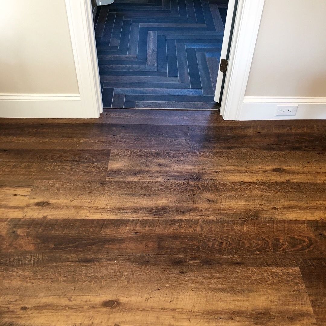 A wooden floor in a room next to a door leading to a bathroom.