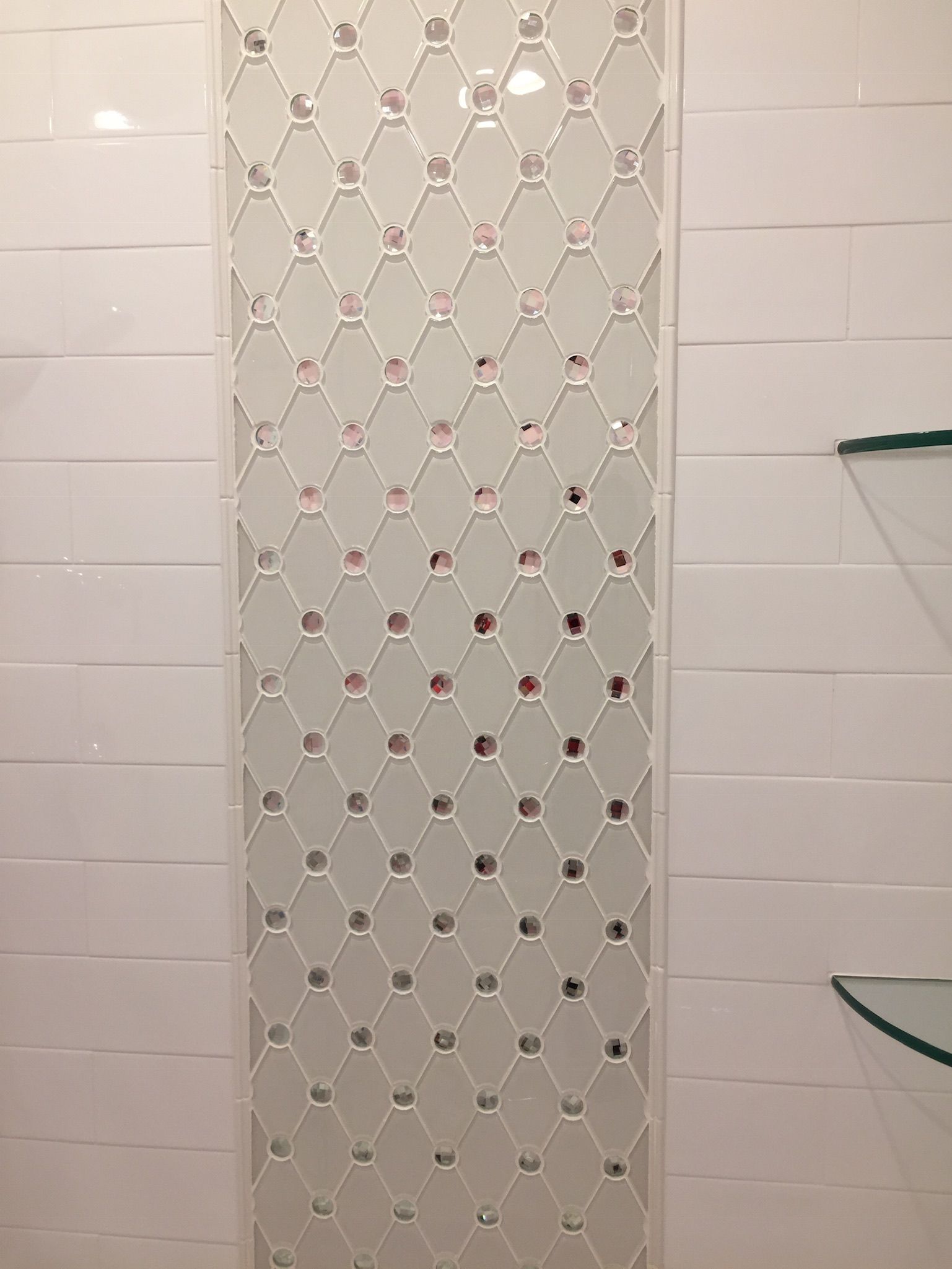 A bathroom with white tiles and a glass shelf.