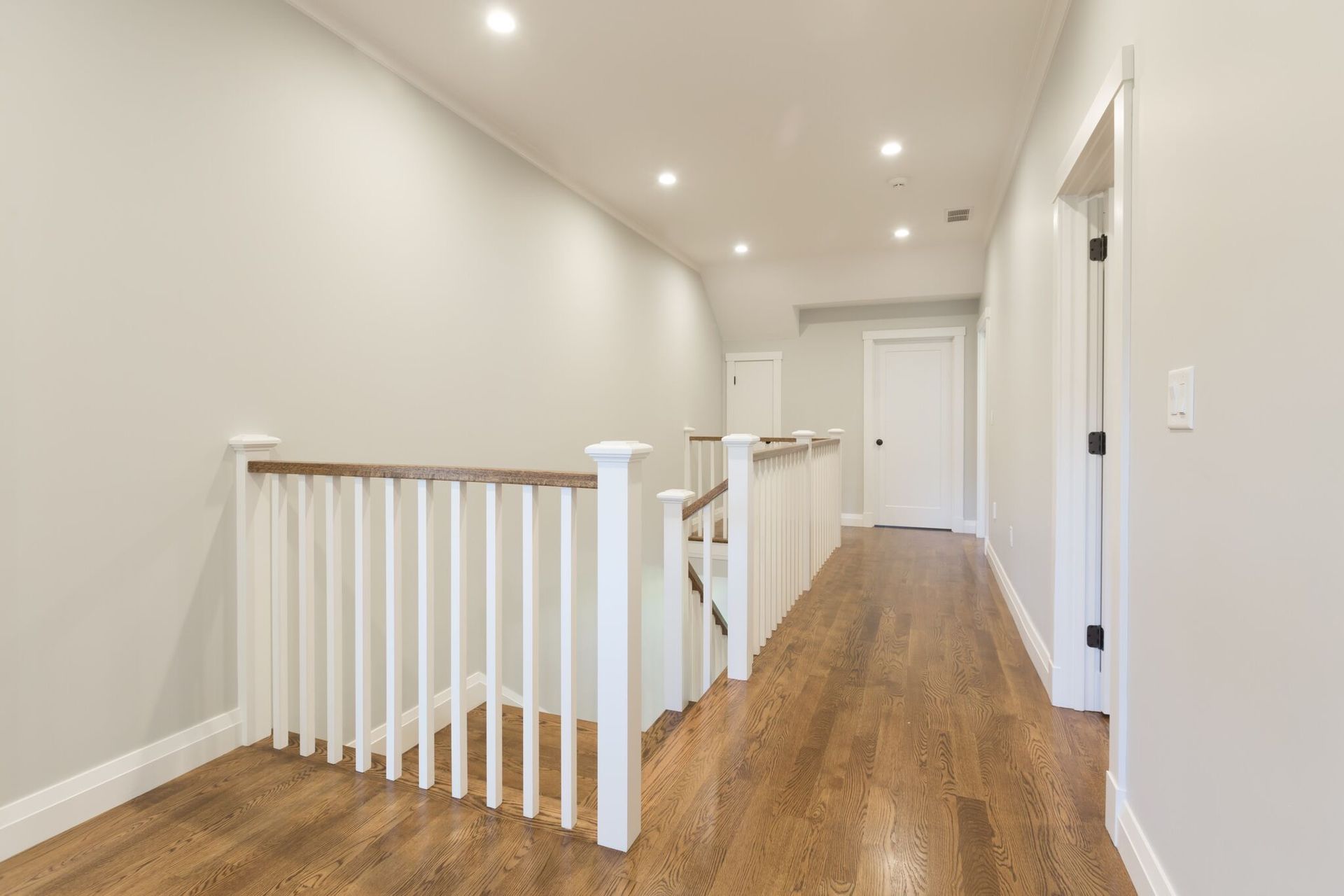 An empty hallway with hardwood floors and stairs in a house.