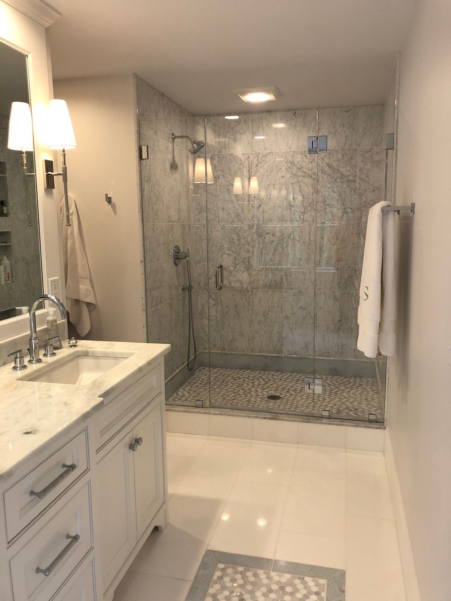 A bathroom with a sink , mirror and walk in shower.