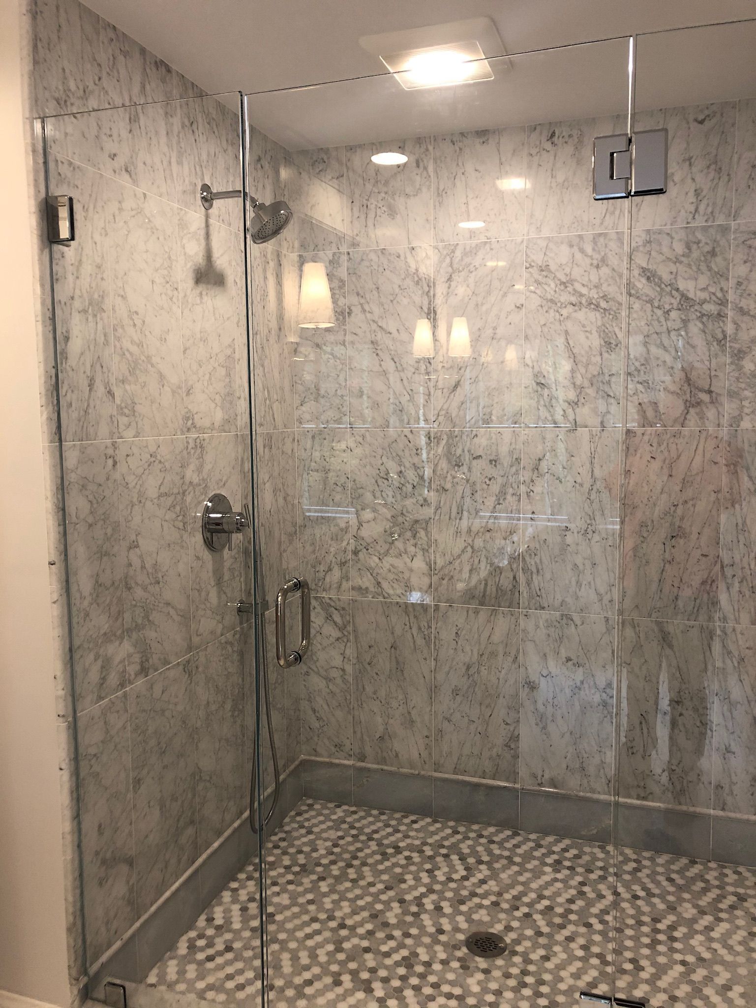 A bathroom with a walk in shower with a glass door and marble walls.