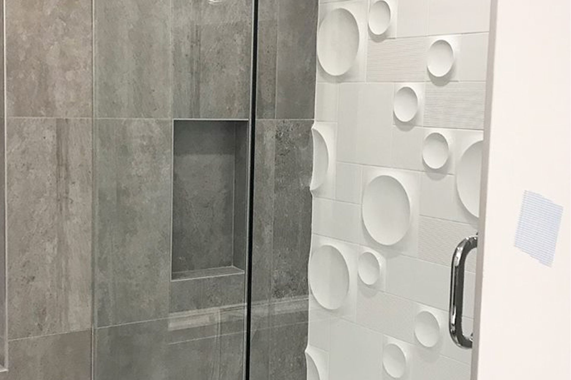 A bathroom with a glass shower door and a tiled wall.
