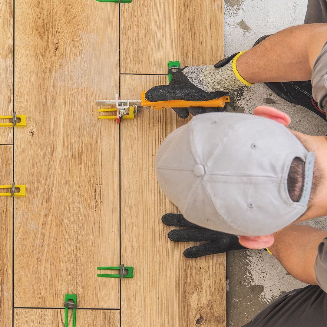 A man is laying tiles on a wooden floor.