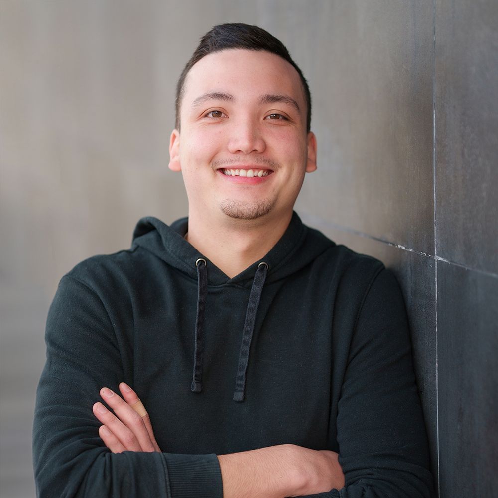 A man in a black hoodie is smiling with his arms crossed