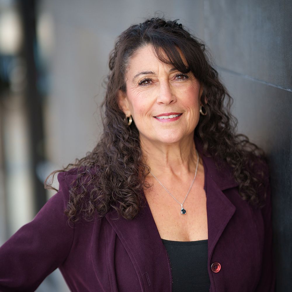 A woman with curly hair is wearing a purple jacket and a black top.