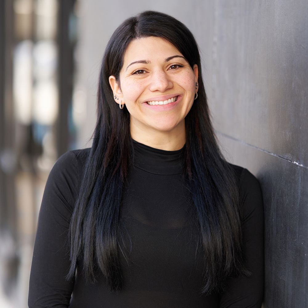 A woman in a black shirt is leaning against a wall and smiling.