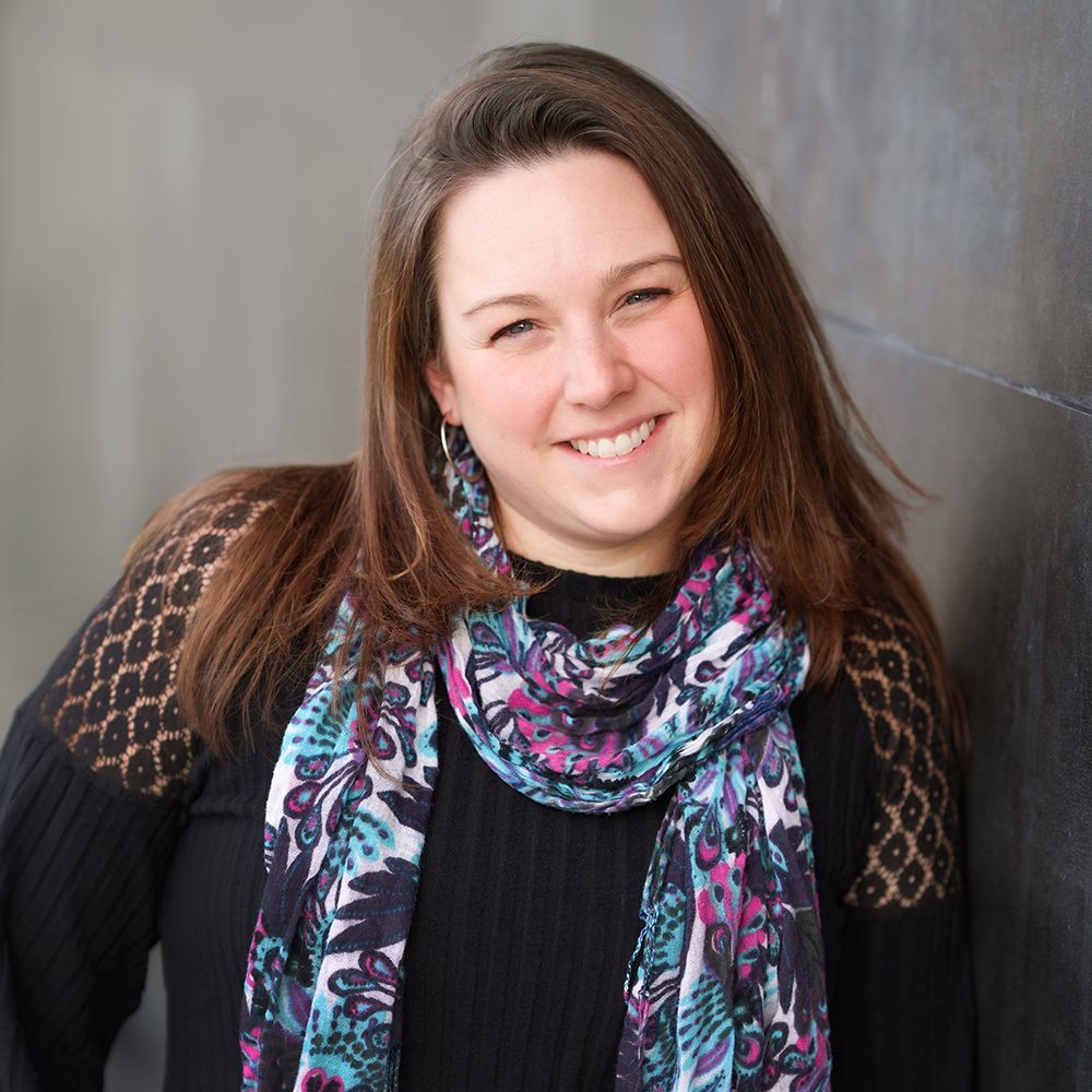 A woman wearing a scarf and a black sweater smiles for the camera