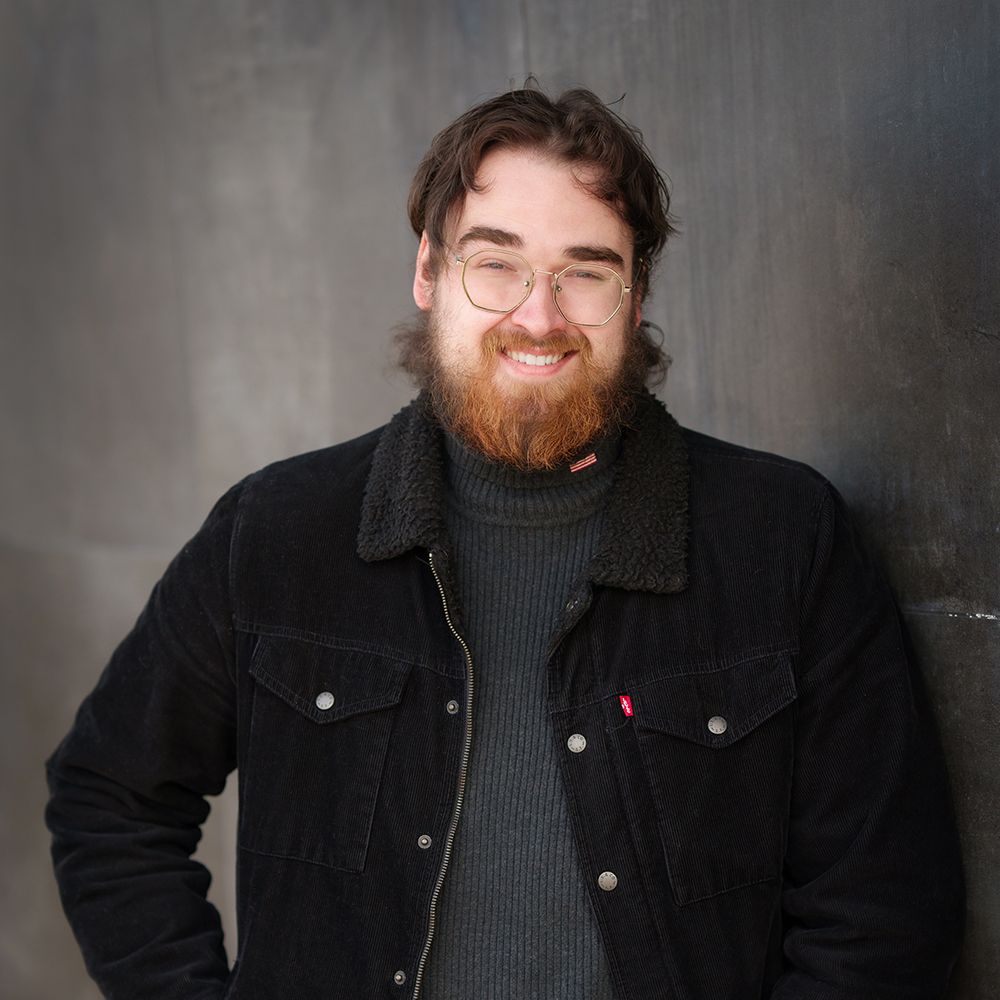 A man with a beard wearing glasses and a black jacket
