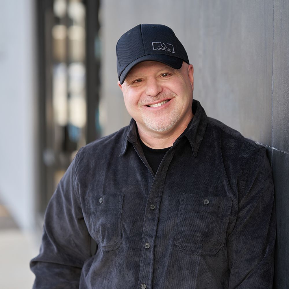 A man wearing a black hat and a black shirt smiles for the camera