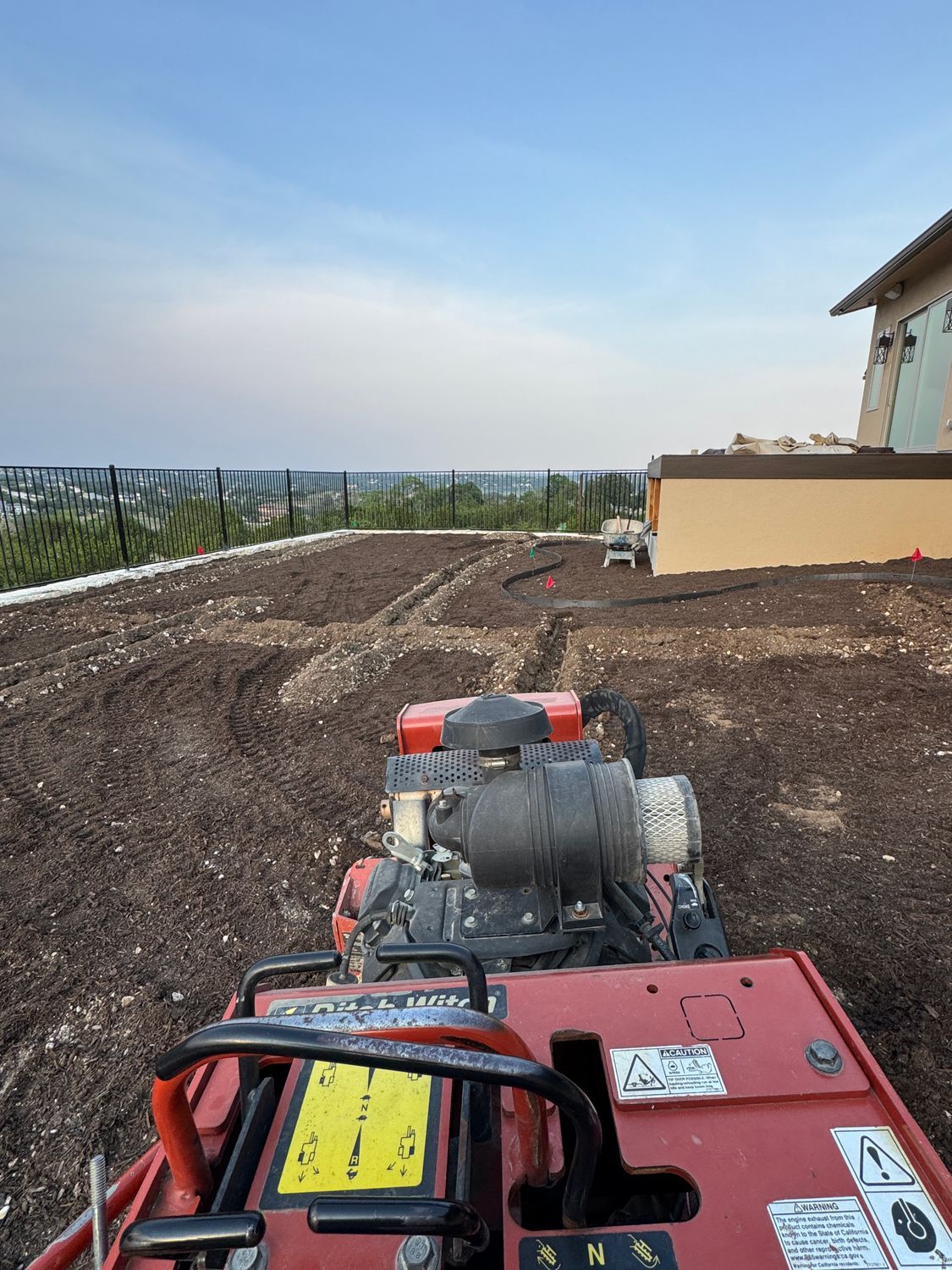 A red compactor compacting soil, with building in the background.
