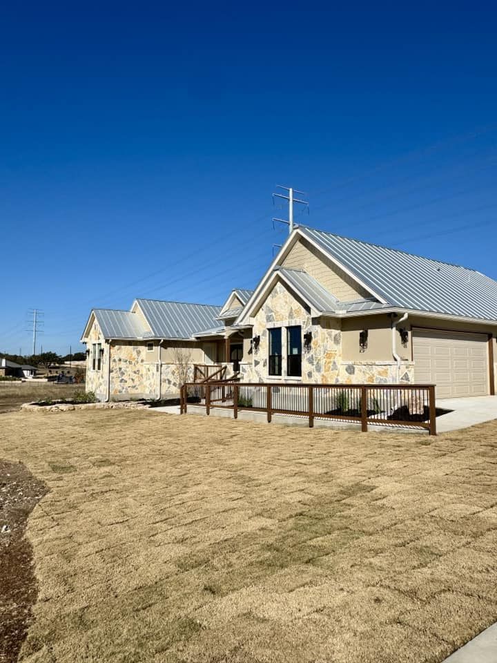 Stone-covered house with metal roof, wooden ramp, and brown yard under a blue sky.