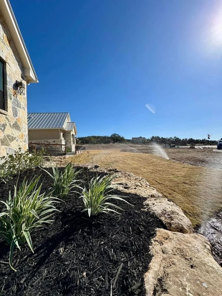 Lawn irrigation watering new grass in front of a house with stone facade on a sunny day.