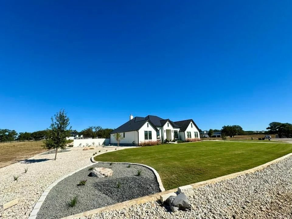 A modern, white house with black trim and a green lawn on a sunny day with blue sky.