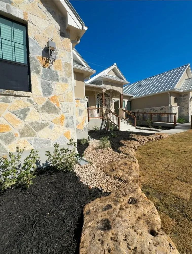 Stone house exterior with a rocky landscape, a porch, and a bright blue sky.