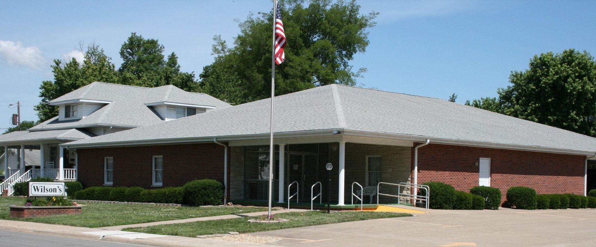 Brick building with flag pole in front; blue sky and trees in background.