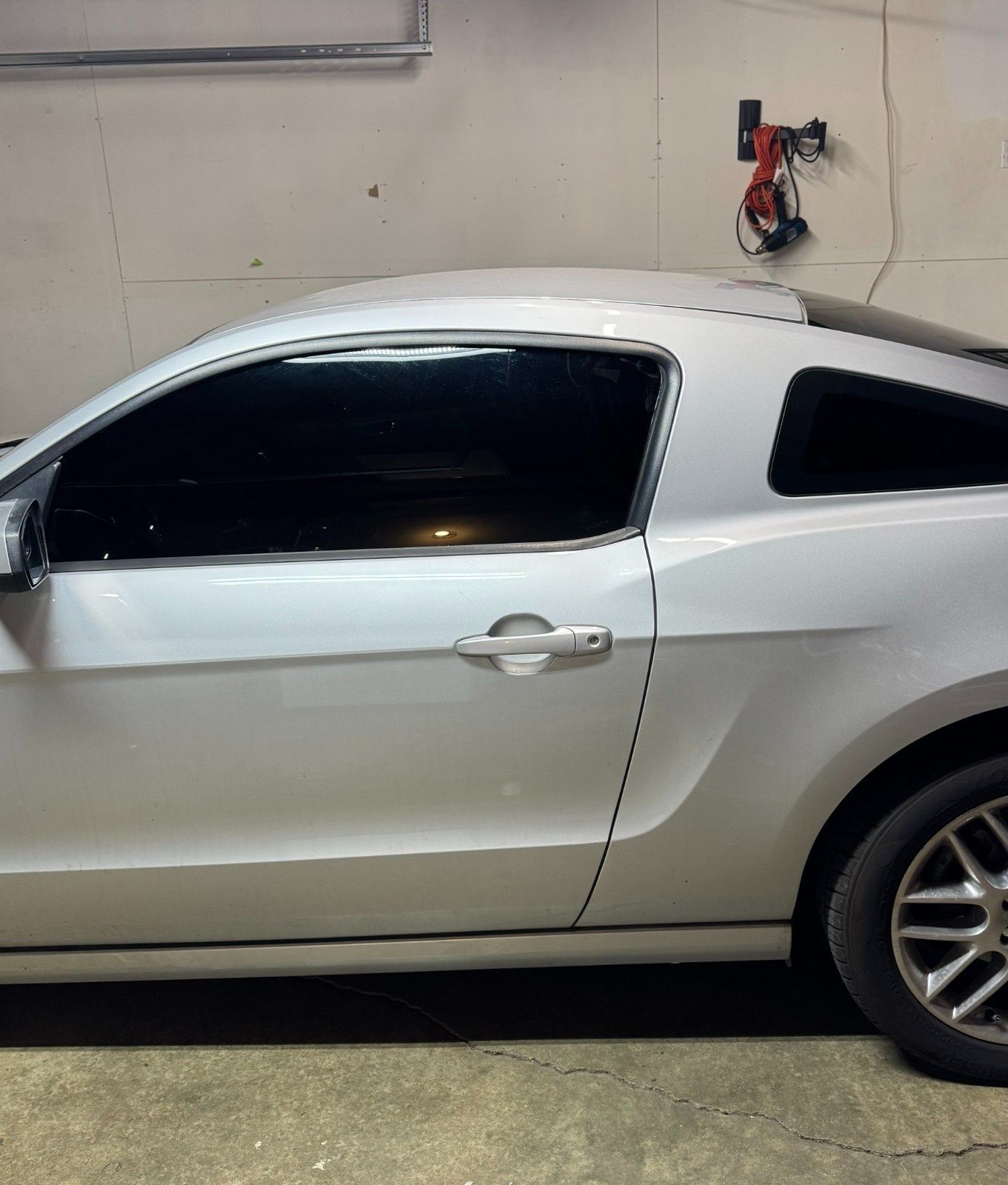 A side view of a white Ford Mustang parked in a garage, featuring dark tinted windows and alloy wheels.