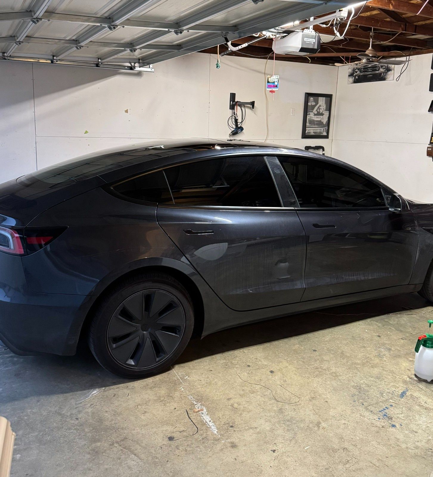 A dark gray Tesla Model 3 parked inside a garage with white walls and a concrete floor.