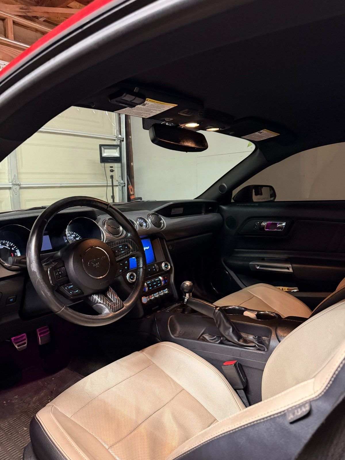 Interior view of a red Ford Mustang with tan perforated leather seats and a manual transmission in a garage.