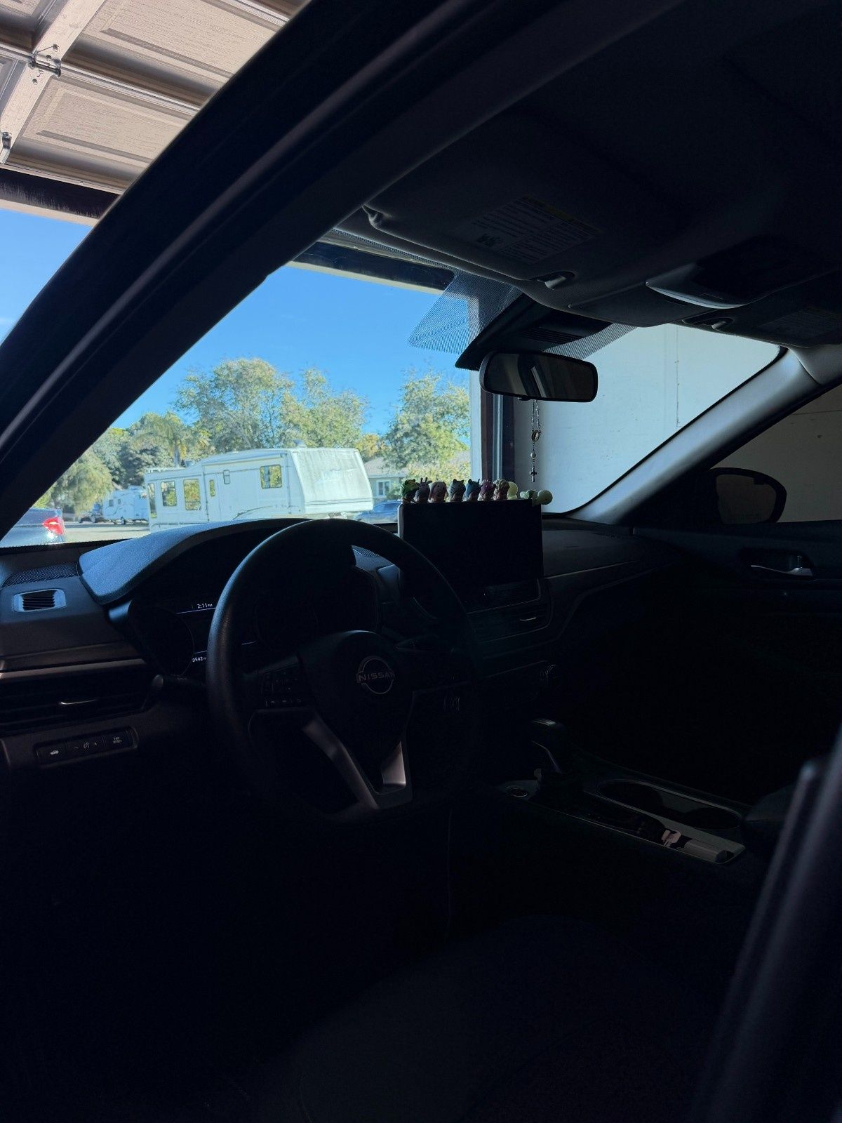 Interior view from a car driver's seat looking out through the windshield at a parking lot with a trailer on a sunny day.