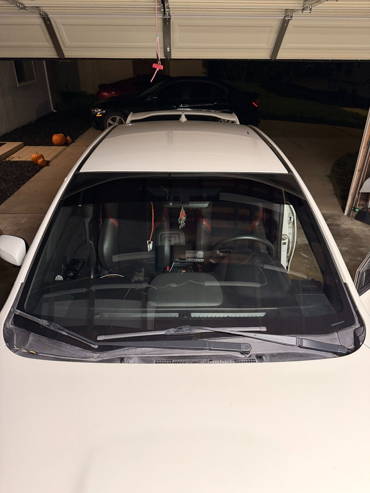 A high-angle view looking through the front windshield of a white car parked inside a garage at night.