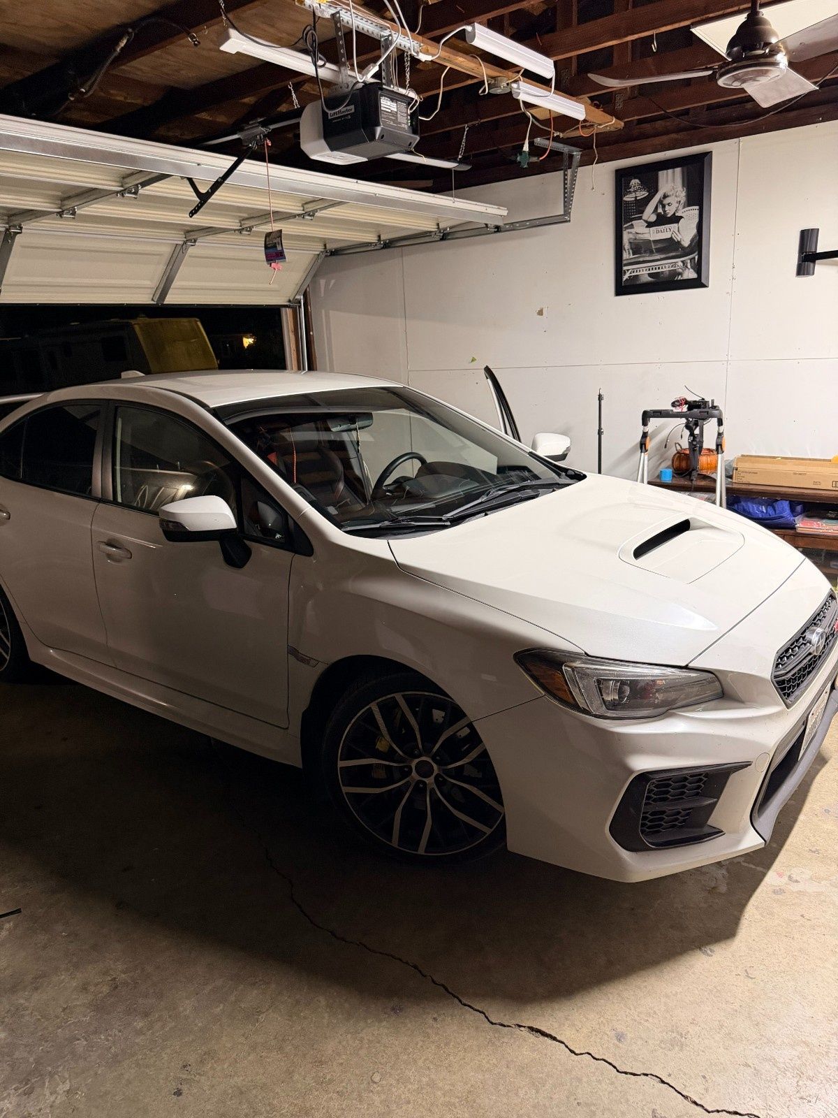 A white Subaru WRX parked inside a home garage, viewed from the front passenger side.