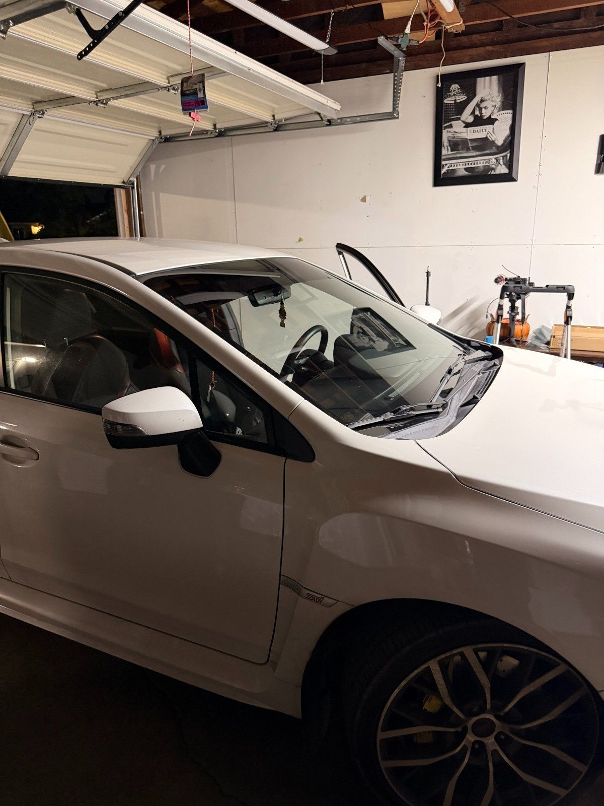 A white car is parked inside a garage, viewed from the front passenger side.