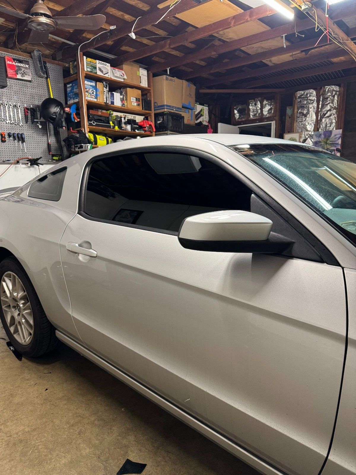 A silver Ford Mustang parked in a garage with dark tinted windows and a visible interior.