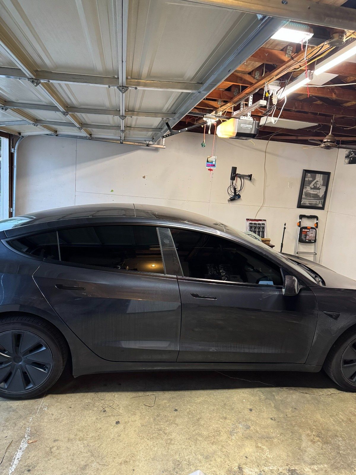 A dark gray Tesla parked inside a cluttered garage.