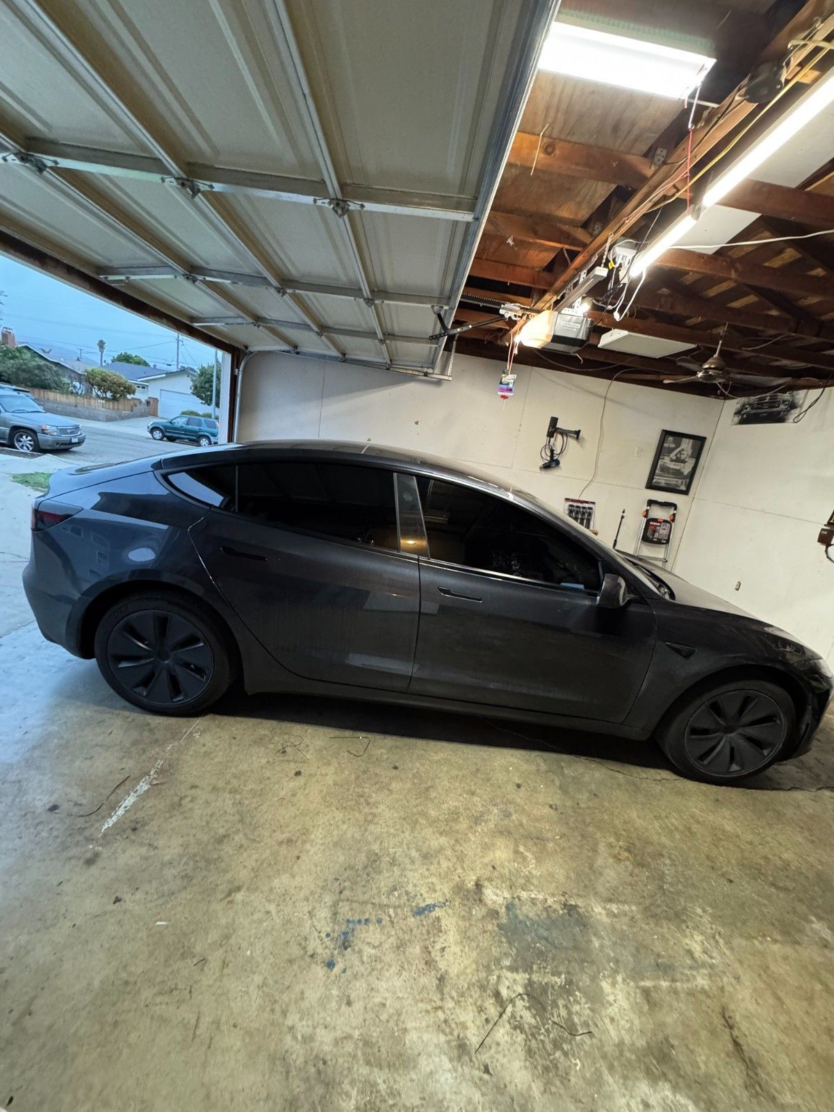 A dark gray Tesla parked inside a residential garage with the door open.