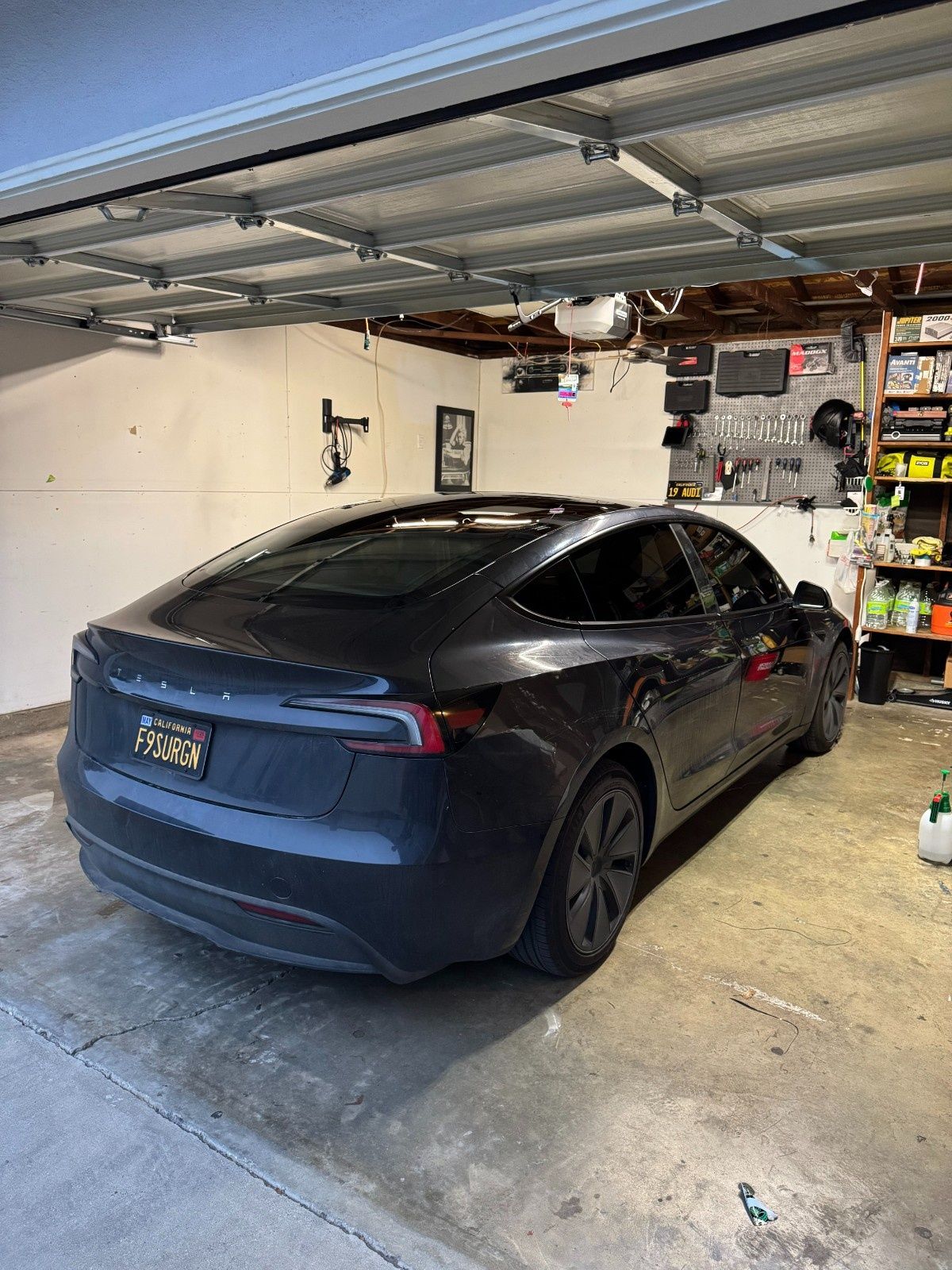 A dark-colored Tesla sedan parked inside a cluttered garage.