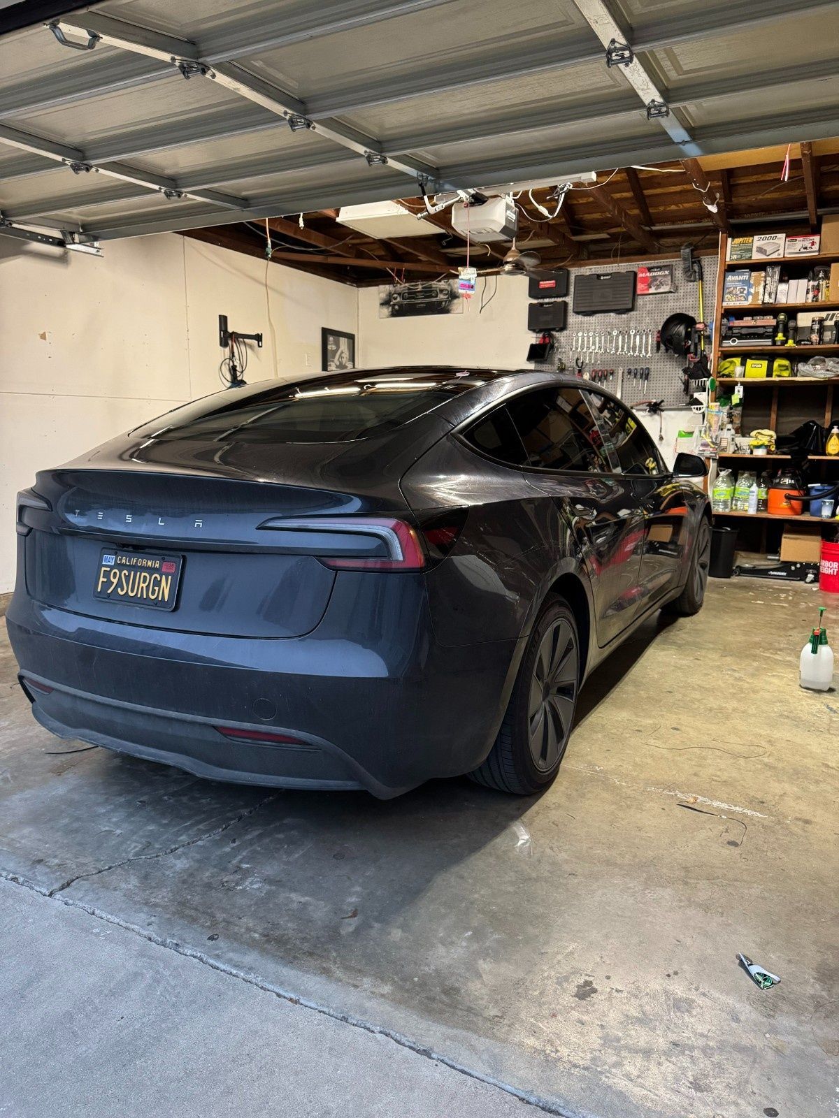 A dark gray Tesla Model 3 parked inside a cluttered residential garage.