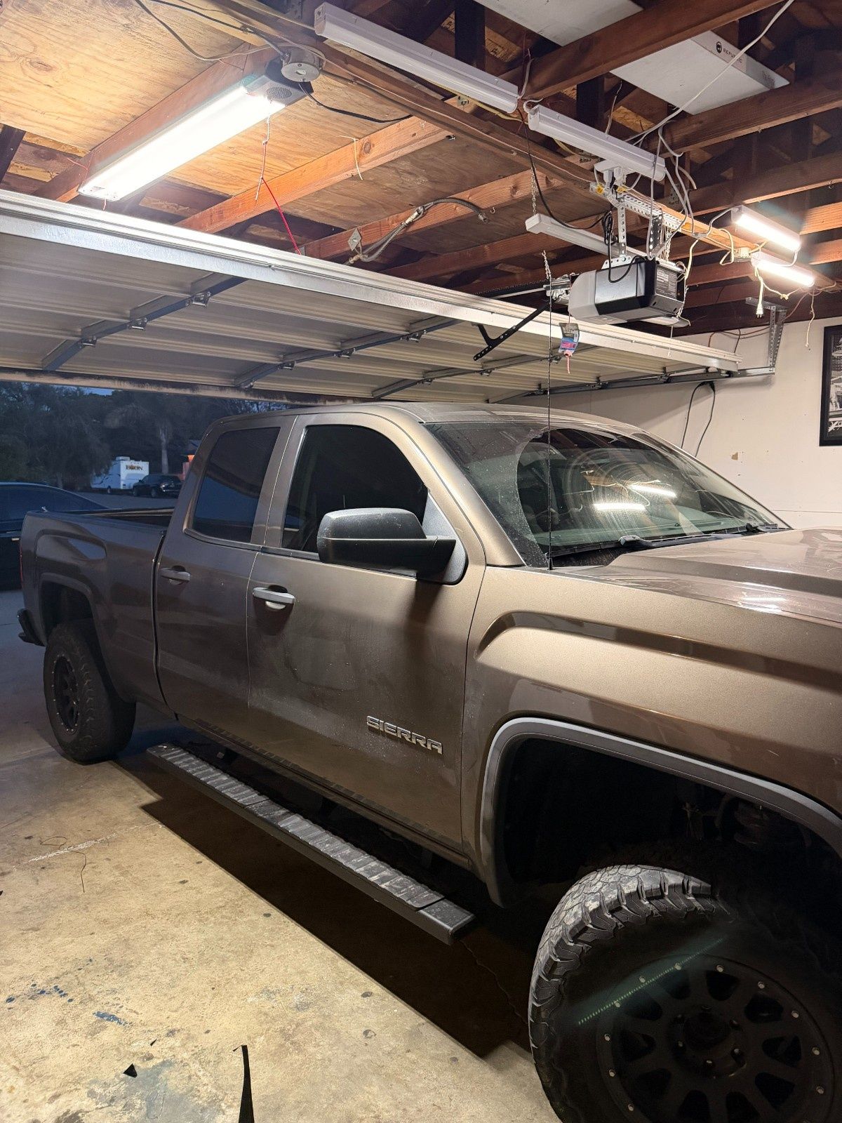 A brown pickup truck parked inside a garage with an open door and overhead lighting.