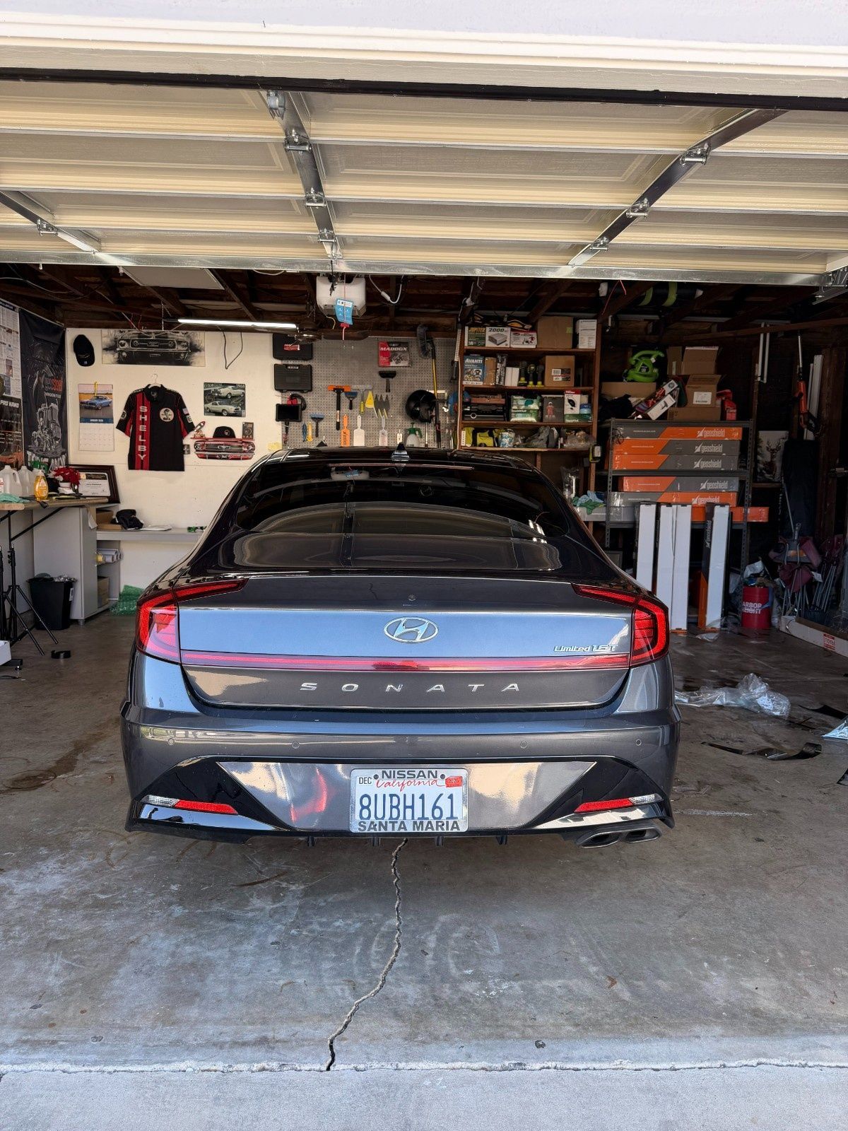 A dark gray Hyundai Sonata parked inside a cluttered residential garage, facing away from the camera.