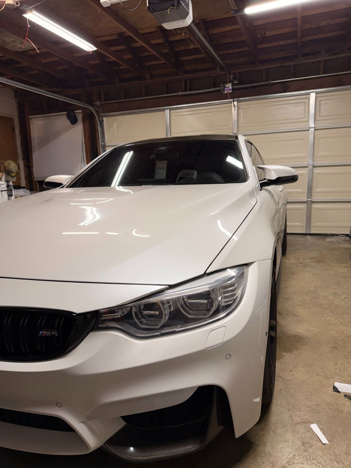 A white BMW M4 sports car parked inside a home garage, featuring a black grille and carbon fiber front splitter.