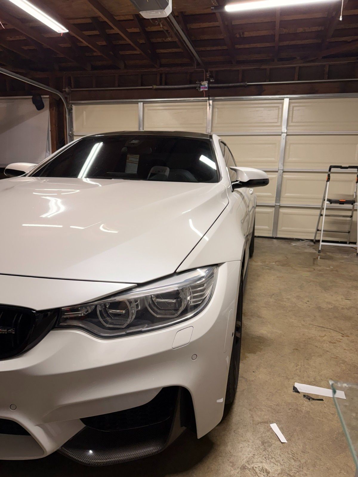 A white BMW parked inside a garage, angled toward the viewer with a ladder nearby.