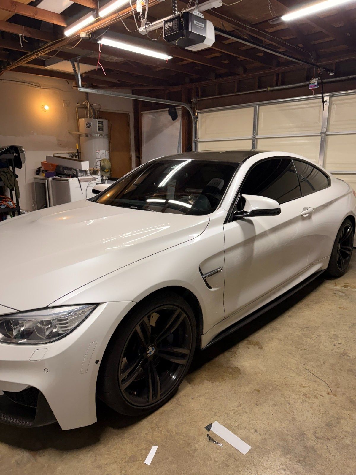 A white BMW M4 coupe with black rims and a dark roof parked inside a garage.