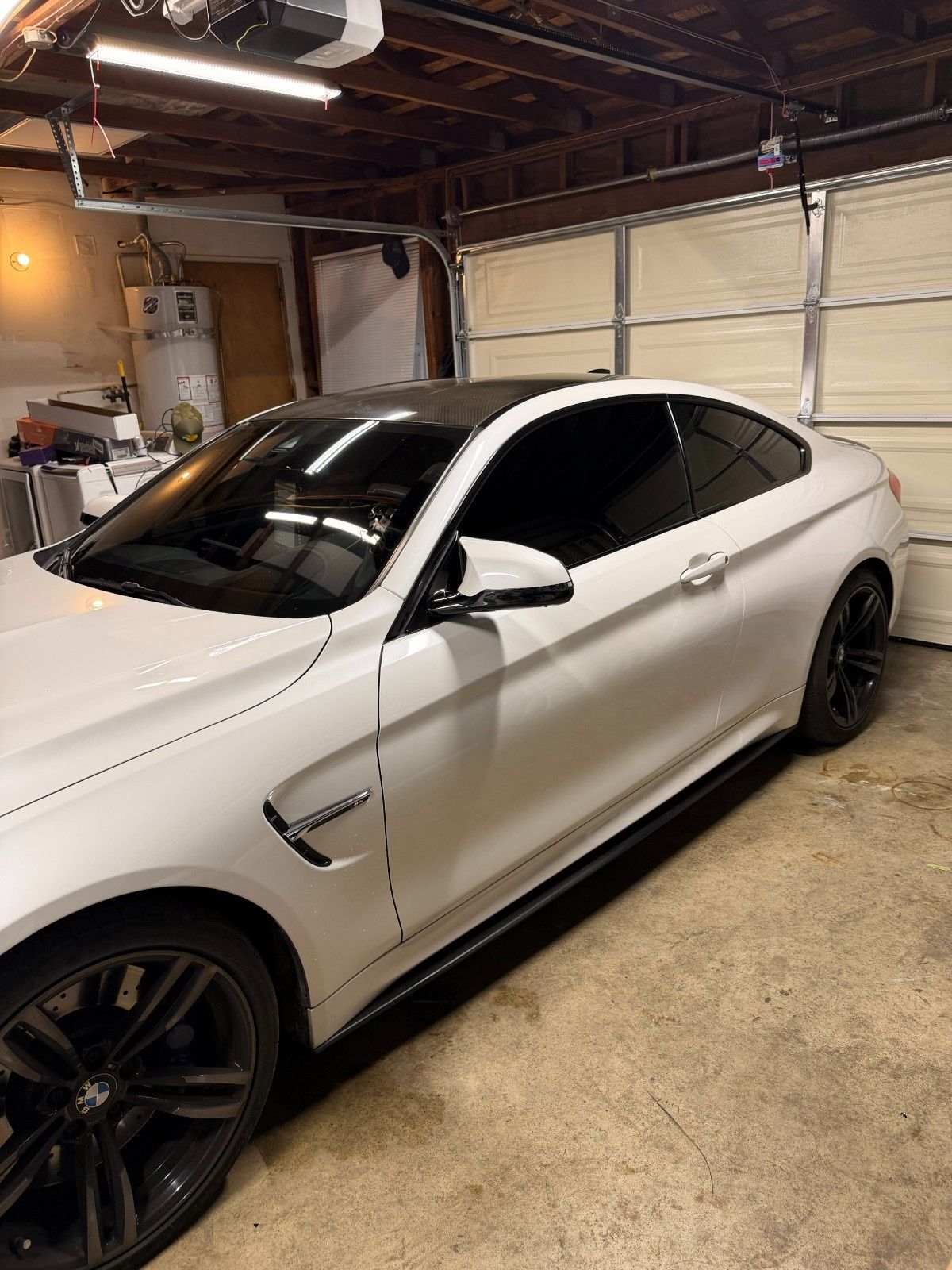 A white BMW M4 coupe with a black roof and tinted windows parked inside a garage.