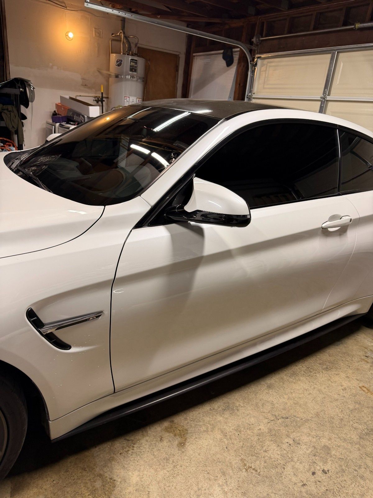 A white BMW M4 coupe parked inside a garage, featuring a black roof, side mirror caps, and dark tinted windows.