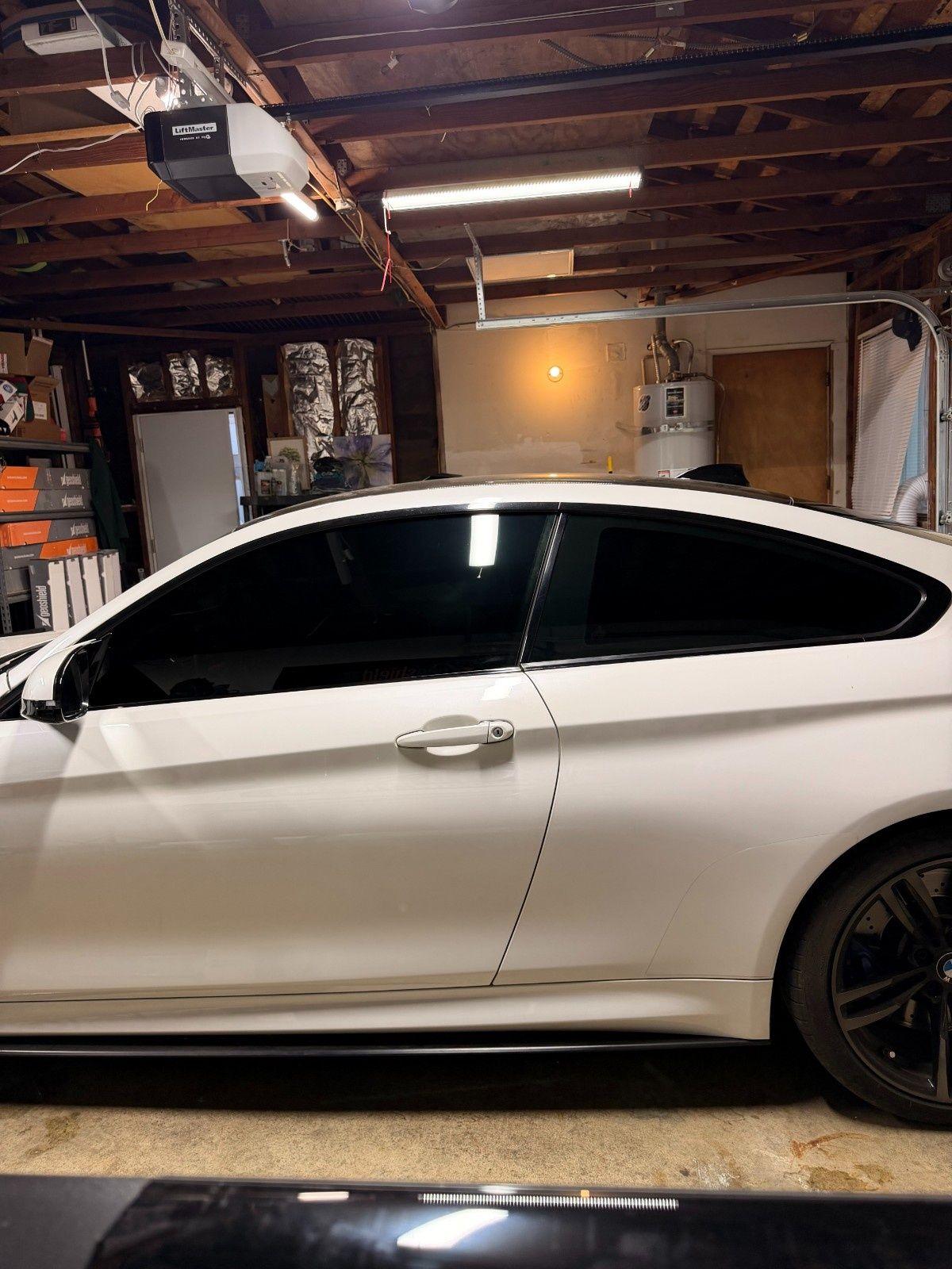 A side view of a white two-door coupe parked inside a dimly lit wooden-beamed garage.