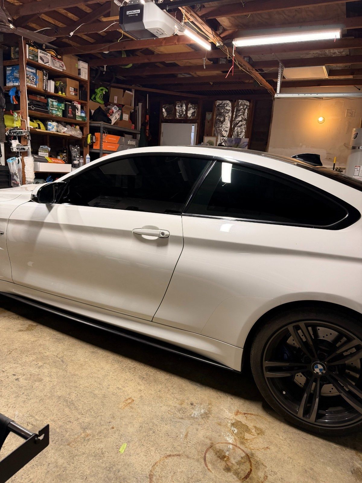 White BMW coupe with tinted windows and black wheels parked inside a cluttered residential garage.