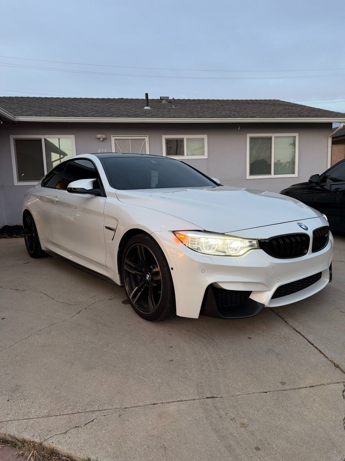 A white BMW M4 coupe parked on a concrete driveway in front of a house.