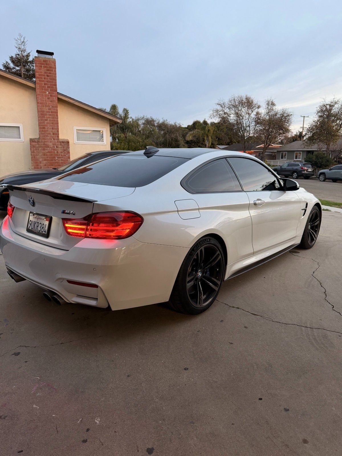A white BMW M4 coupe parked on a residential driveway, viewed from the rear three-quarter angle.