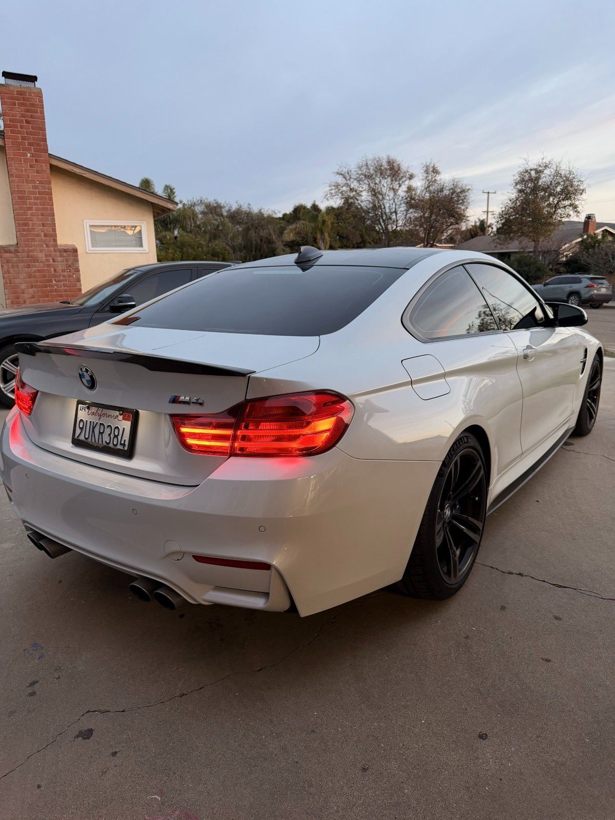 A white BMW M4 coupe parked on a driveway during twilight, featuring a black roof, spoiler, and dark wheels.