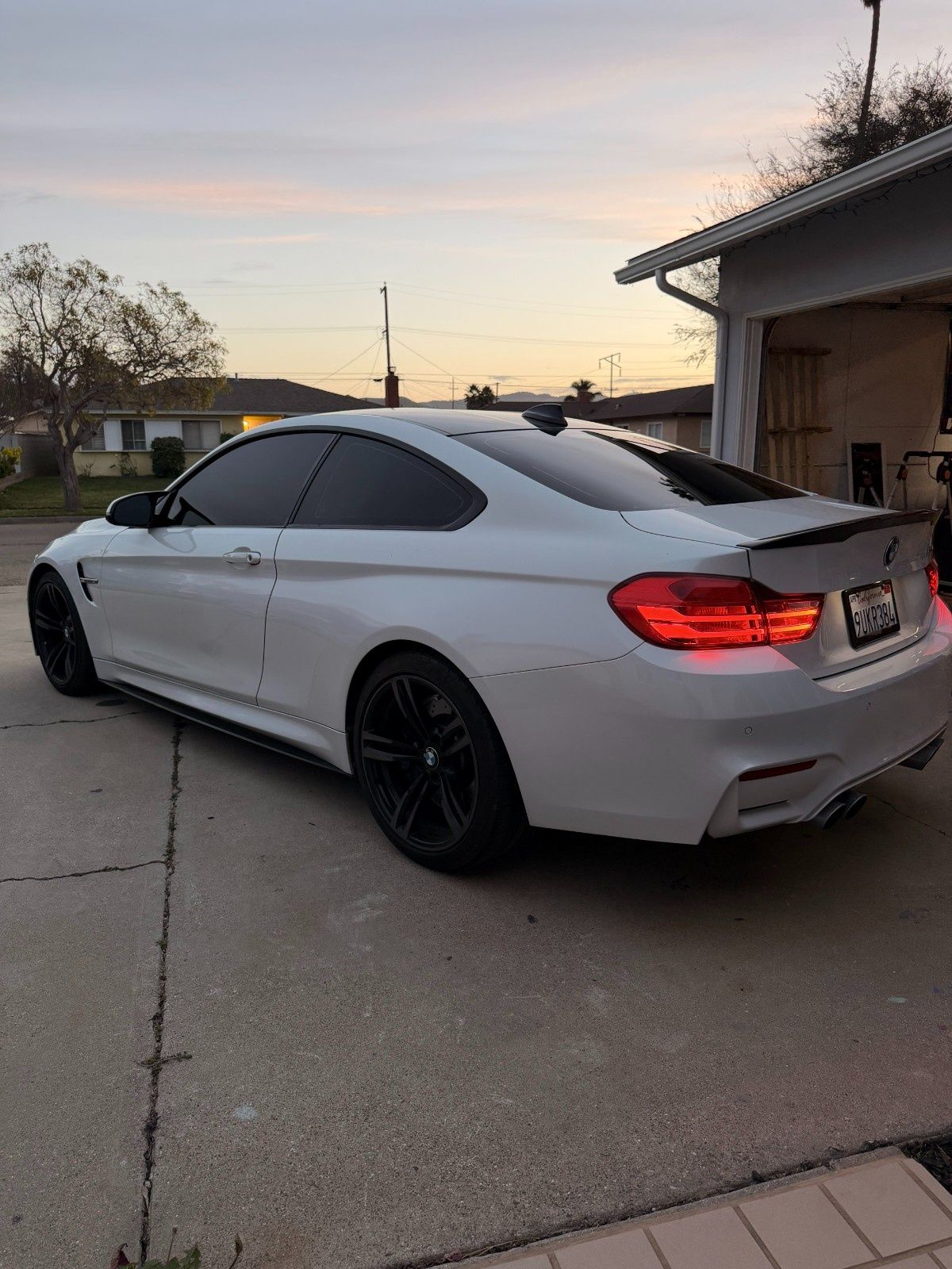 A white BMW M4 coupe parked on a concrete driveway during sunset, featuring tinted windows and black wheels.