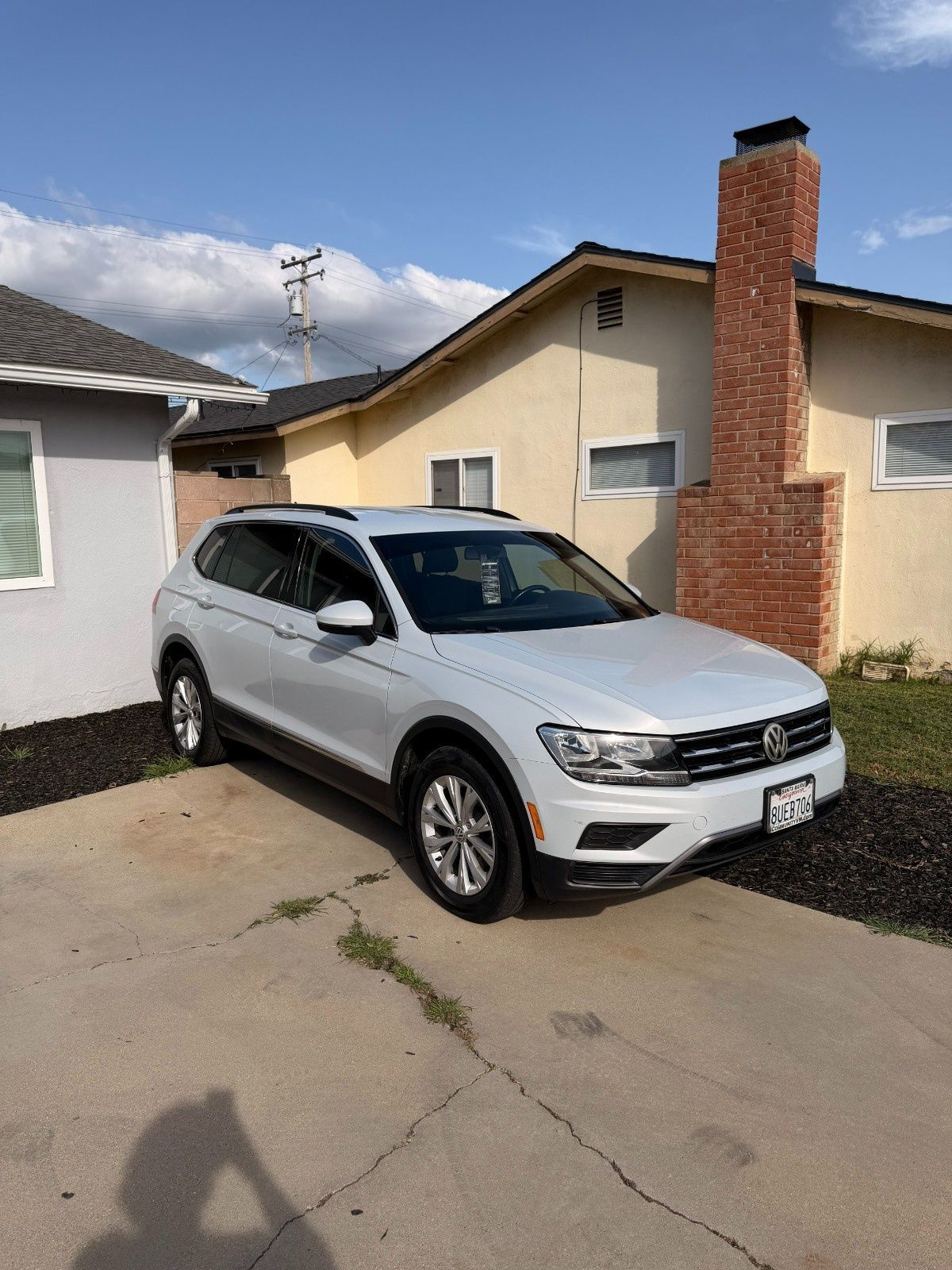A white Volkswagen Tiguan parked on a concrete driveway in front of a light-colored house with a brick chimney.