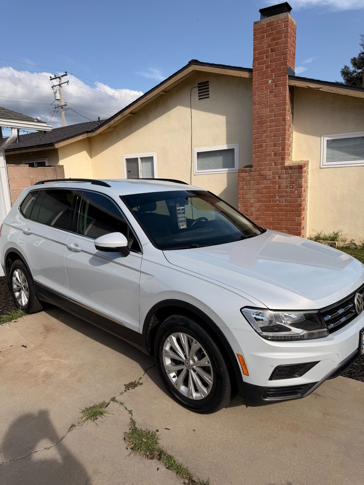 A white Volkswagen Tiguan SUV parked in a concrete driveway in front of a house with a brick chimney.