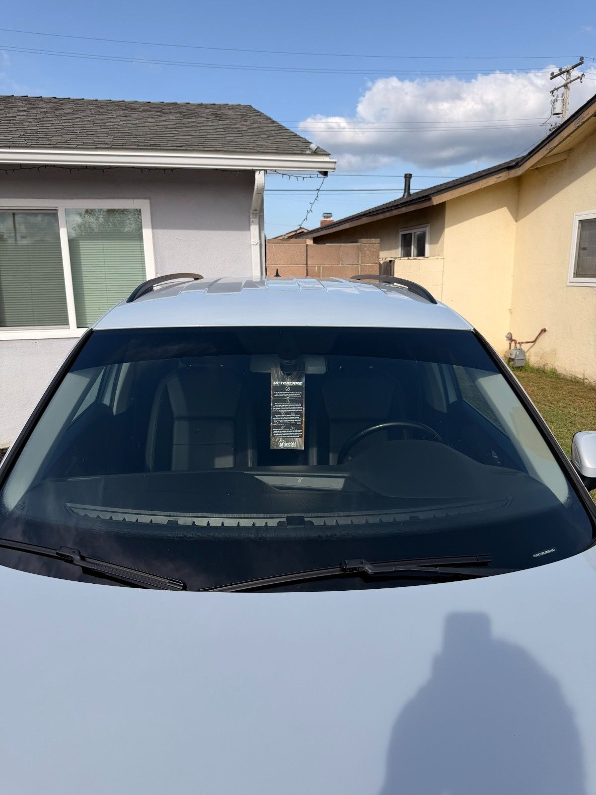A light-colored car parked outdoors between two houses, viewed from the front windshield looking into the interior.
